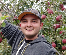 A teenager standing in front of apple trees, smiling
